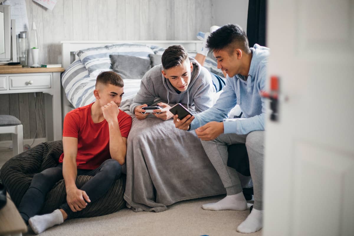Intensivpädagogische Verselbstständigung bei der Karl Immanuel Kuepper-Stiftung - drei männliche Jugendliche sitzen in einem Zimmer zusammen und schauen sich gemeinsam Inhalte in einem Smartphone an